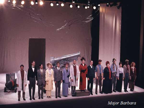 A group of actors stands in a line on stage taking a bow. They are dressed in various costumes, and there's a large prop resembling a cannon behind them. Stage lights illuminate the scene. The text "Major Barbara" is on the bottom right corner.