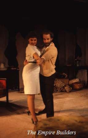A man and woman dressed in mid-20th-century attire dance closely on a stage with a dimly lit, simple set. The woman wears a white dress and the man is in a beige sweater. Text at the bottom reads "The Empire Builders.