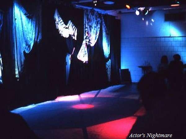 Dimly lit stage with a dark curtain backdrop and subtle blue and red spotlights. Silhouetted figures are partially visible, with "Actor's Nightmare" written in the bottom right corner.