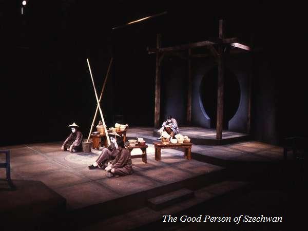 Theater stage scene featuring three actors in dim lighting, sitting around wooden furniture with long poles nearby. The backdrop includes a circular and rectangular wooden structure. "The Good Person of Szechwan" is written in the corner.