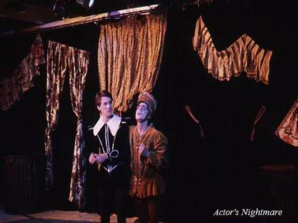 Two actors in period costumes stand on stage. The one on the left wears a black outfit with a white collar, while the other wears a brown outfit and hat. They are under stage lights with curtains in the background. Text reads "Actor's Nightmare.