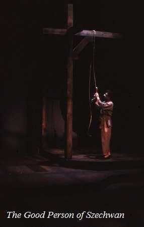 A person on stage stands beside a tall wooden structure holding a rope, in a dimly lit scene from a theatrical performance titled "The Good Person of Szechwan.