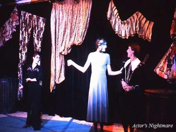 Three actors on stage under dramatic lighting, with two wearing light-colored costumes and one in dark. The background is decorated with hanging fabric. The setting has a theatrical, dreamlike atmosphere. Text reads "Actor's Nightmare.