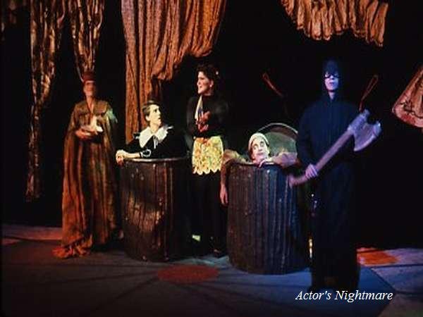 A theatrical stage with actors in costume. One stands holding a large axe, while others appear to be in barrels. The background features draped fabric. The text "Actor's Nightmare" is visible.