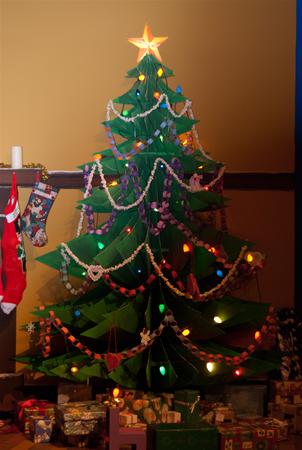 A decorated Christmas tree with a star on top, adorned with colorful lights and paper chains. Stockings hang nearby, and presents are arranged beneath the tree.