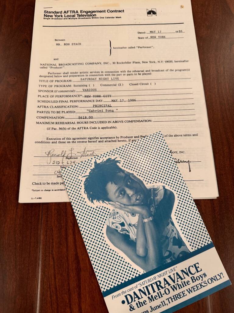 A signed contract from the National Broadcasting Company dated May 17, 1986, is on a wooden table. Below it is a black and white flyer for "DANITRAVANCE & the Mell-O White Boys," advertising a three-week event in June.