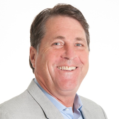 Chris Coborn, a smiling middle-aged man with short brown hair, wearing a light gray blazer and light blue shirt, pictured against a plain white background.